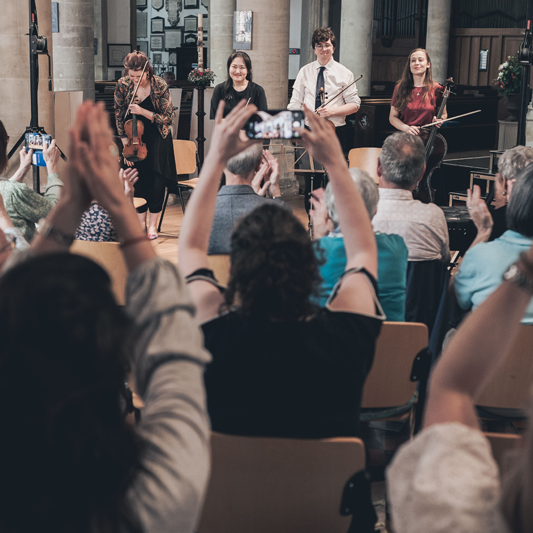 Image shows an audience watching 4 musicians